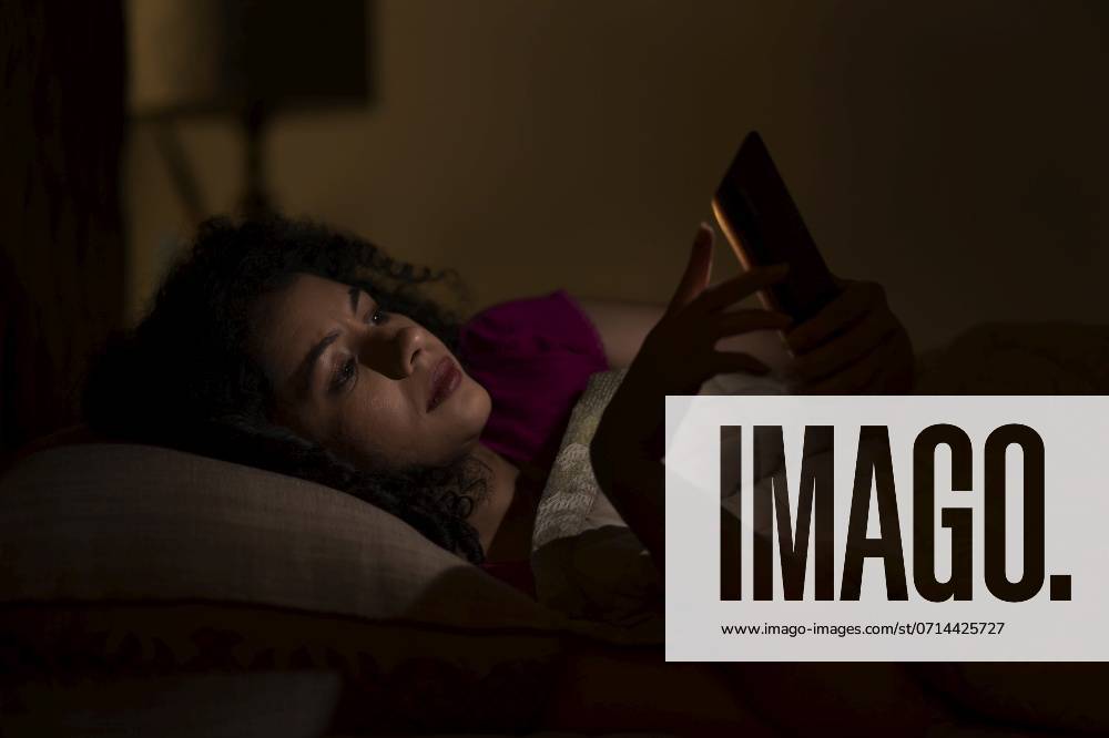 Woman Chatting on smartphone at night while lying on bed ,model released, Symbolfoto