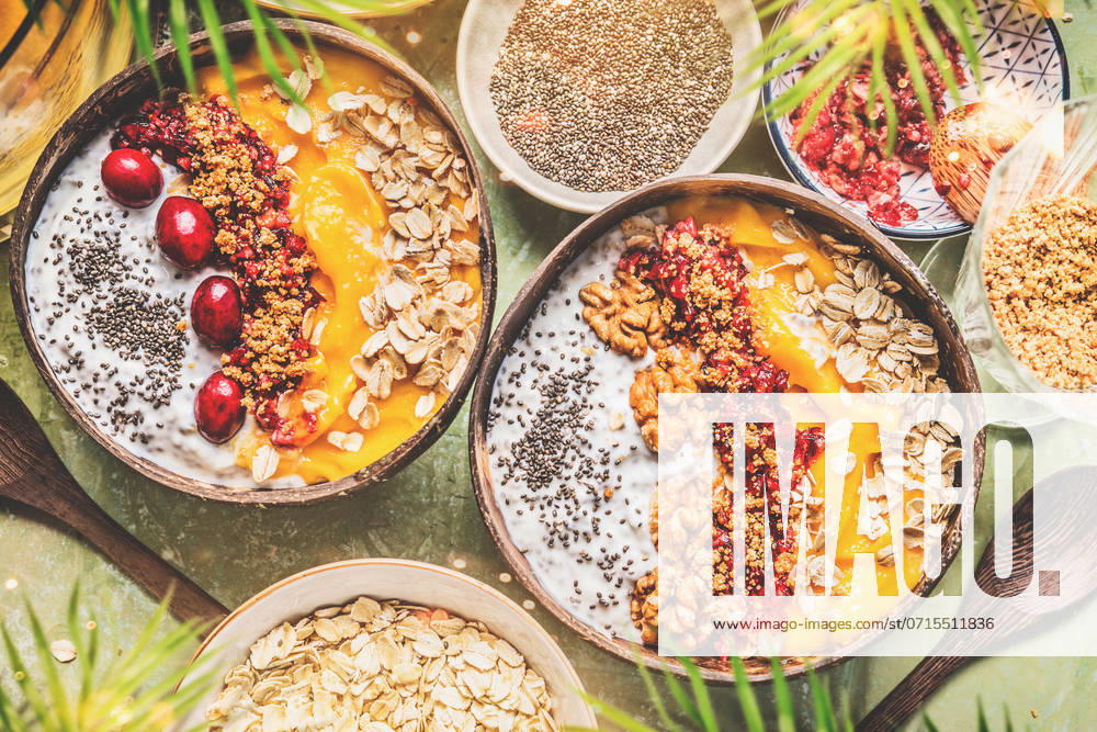 Smoothie mango bowls with chia seeds yogurt pudding and cranberries, nuts, oatmeal topping in coconut shells with spoon, top view. Healthy clean breakfast food ,model released, Symbolfoto
