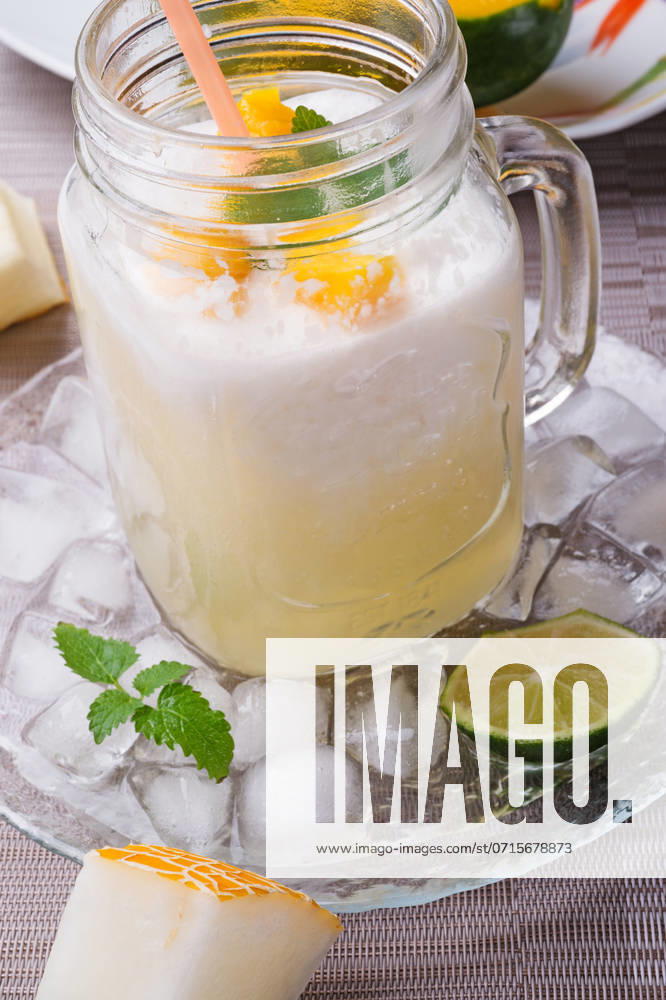 Fresh vegetarian tropical melon cocktail with coconut milk and mango. served in transporant cup with ice, fresh melon, mango, lime, melissa and coconut milk on grey napkin. close up ,model released, Symbolfoto