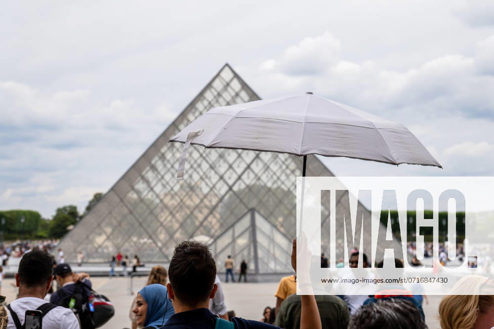 Vor dem Louvre-Museum in Paris schützen sich Touristen mit einem Sonnenschirm vor der Hitze im Sommer, während sie in der Warteschlange vor der berühmten Glaspyramide stehen