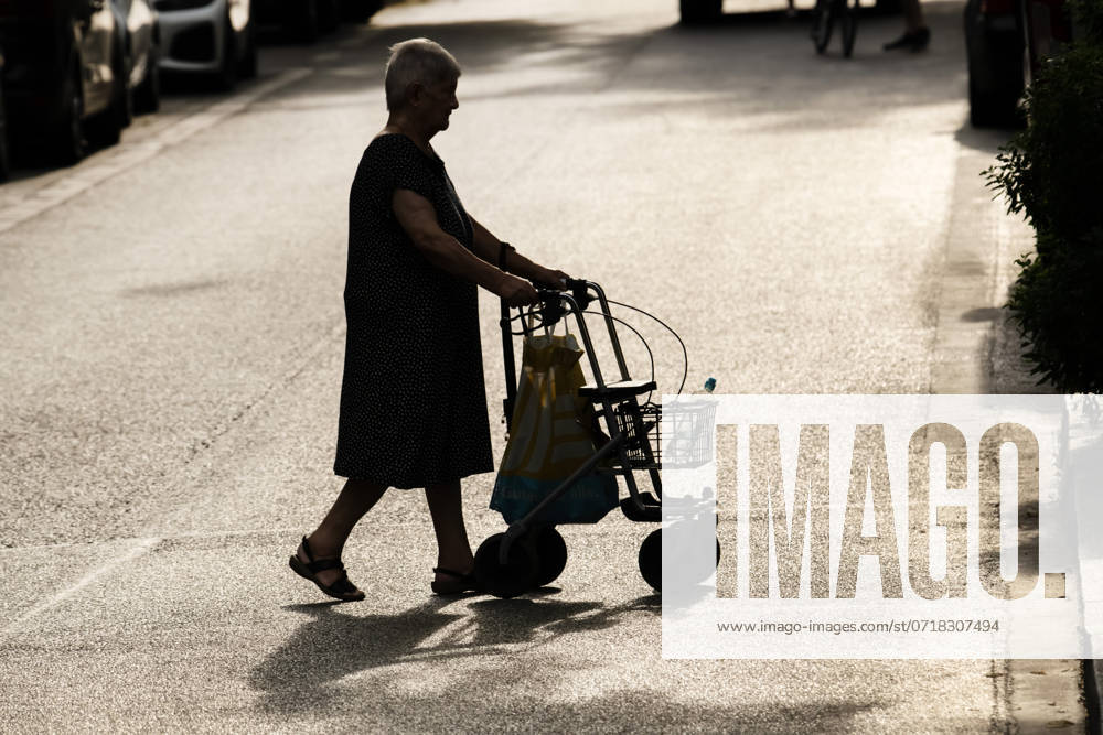 IMAGO Creative, Jahreszeit Sommer, Hitze alte Frau mit Rollator bei Sommerhitze in der Stadt unterwegs, Juli 2024 Deutschland, München, Juli 2024, alte Frau mit Rollator in der Hitze unterwegs, bei der Sommerhitze besteht vor allem für ältere Menschen die Gefahr der Dehydrierung, Seniorin hat Wasserflasche mitgenommen, starkes Sonnenlicht, Gegenlicht, Silhouette, Symbolfoto Rente, Rentner, Senioren, Leben im Alter, eingeschränkte Mobilität, Bewegung, Selbstständigkeit im Alter,
