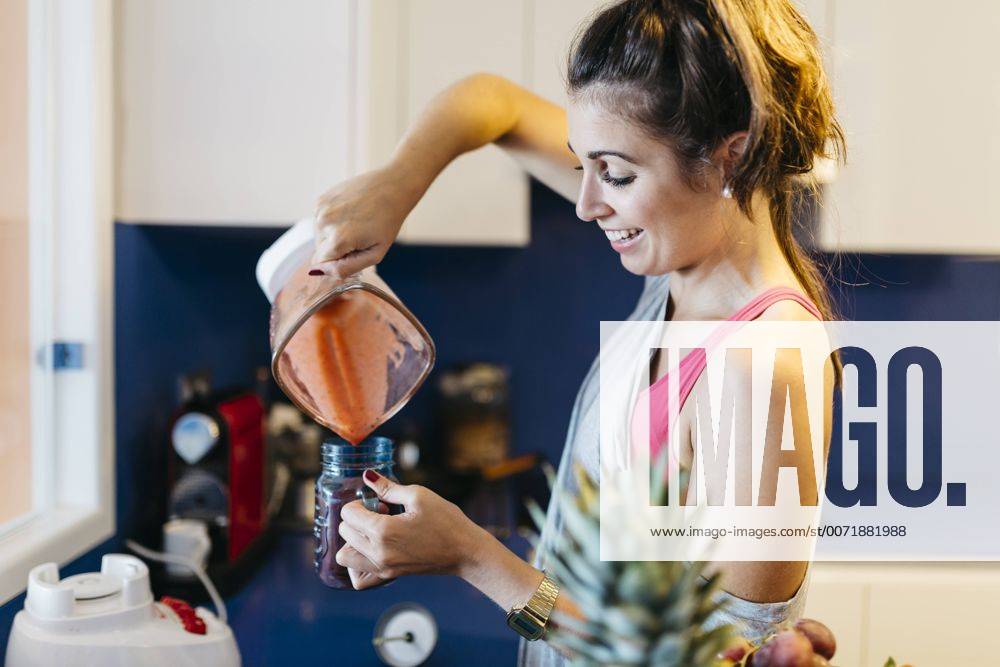 Smiling young woman in kitchen pouring smoothie into mug model released Symbolfoto property released JRFF000736