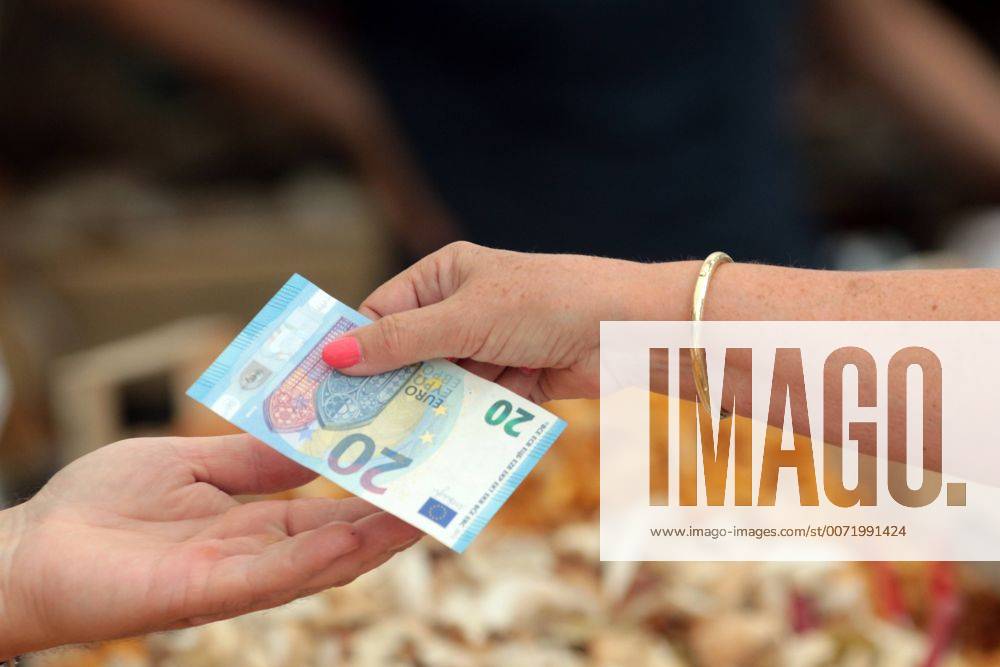 Frau reicht einer Marktverkäuferin einen Euro Geldschein zum Bezahlen ihrer gekaufter Ware; Viktualienmarkt in München, Bayern, Deutschland
