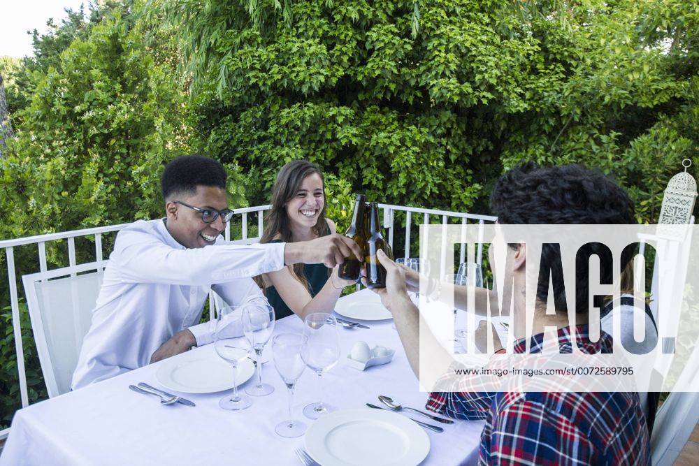 IMAGO Creative: Gesellschaft, Integration Friends toasting with bottles of beer during a summer dinner model released Symbolfoto property released ABZF000722