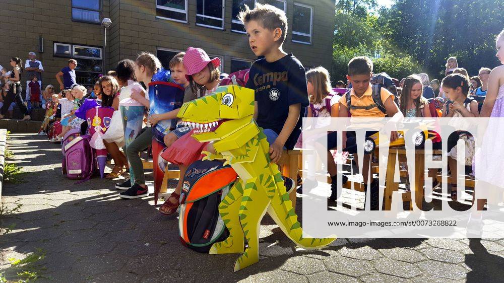 I-Maennchen bei der Einschulung mit Ihren Schultueten auf dem Schulhof, im Vordergrund ein Kind mit Dinosaurier-Schultuete, Deutschland first-grader with their first day at school with school cones on the schoolyard, Germany BLWS435872
