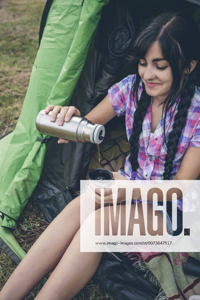 Young woman sitting in a tent pouring coffee from thermos flask into cup, partial view model released Symbolfoto DAPF000262