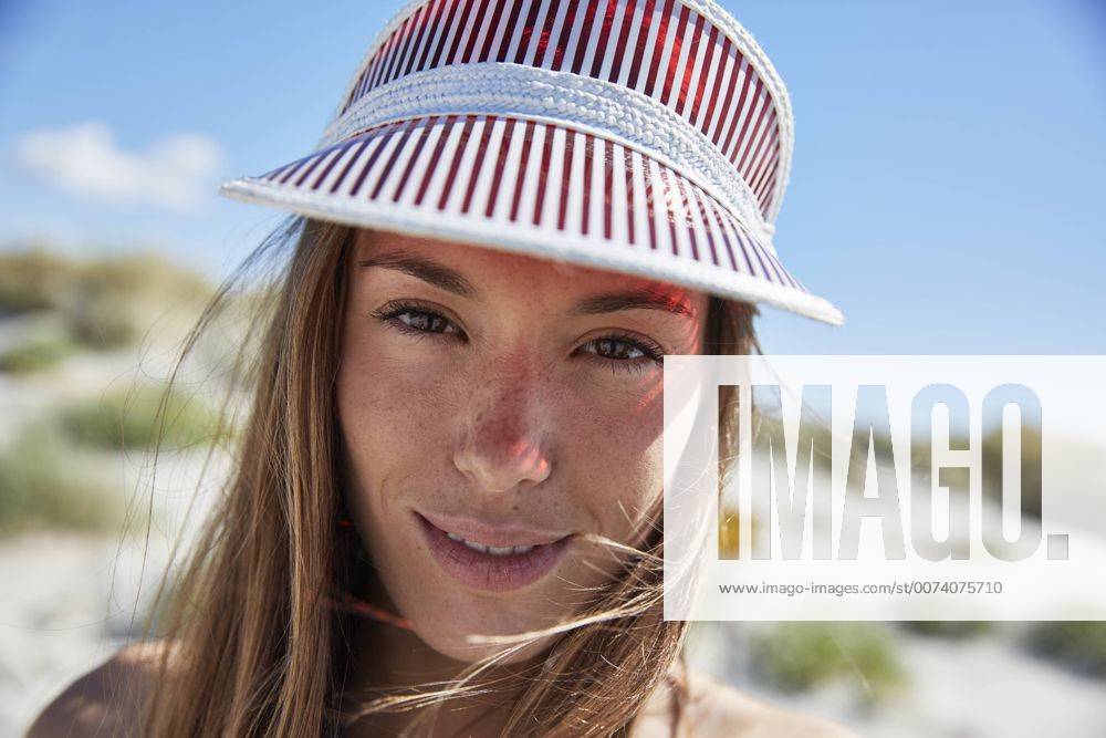 IMAGO Creative, Jahreszeit Sommer, Sonnenschutz Portrait of smiling young woman wearing sun visor on the beach model released Symbolfoto SRYF000054