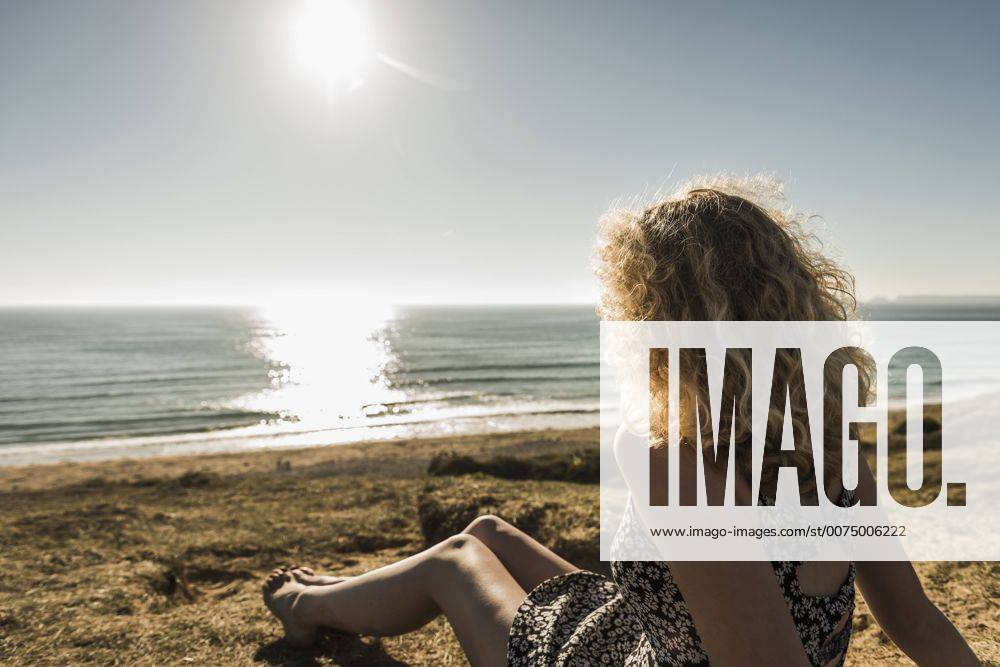 Back view of teenage girl sitting on the beach at evening twilight looking to the sea model released Symbolfoto UUF08741