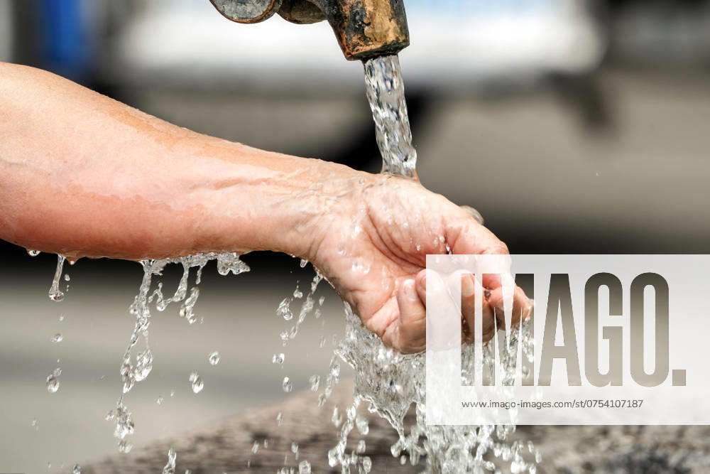 IMAGO Creative, Jahreszeit Sommer, Hitze Abkühlung am Brunnen, Frau lässt kaltes Wasser über ihr Handgelenk laufen, Hitzewelle, München, August 2024 Deutschland, München, August 2024, eine Frau lässt kaltes Wasser über Arm und Handgelenk laufen, die Sommerhitze ist brutal, das Brunnenwasser verspricht Abkühlung in der Hitzewelle, Temperaturen über 30 Grad, Rekordhitze, Sommerwetter, Hochsommer, Sommer, Bayern,