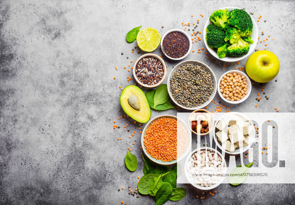 Vielfalt an nährstoffreichen Lebensmitteln für Veganer mit Kopierfläche: Bohnen, Linsen, Quinoa, Tofu, Gemüse, Nüsse, Kichererbsen, Reis, Avocado, Obst, Steinhintergrund, Draufsicht. Gesunde vegetarische Ernährung Variety of nutrient-rich food for vegans with copy space: beans, lentils, quinoa, tofu, vegetables, nuts, chickpeas, rice, avocado, fruit, stone background, top view. Healthy vegetarian nutrition