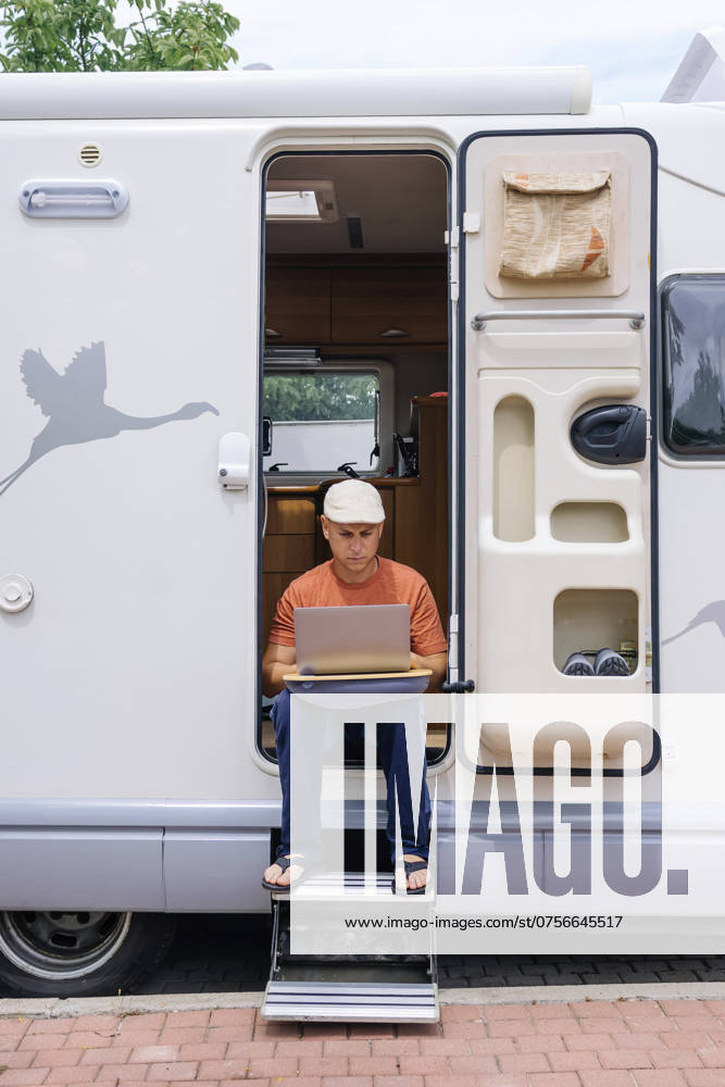 Freelancer using laptop and sitting on doorway of motor home model released, Symbolfoto property released, JCMF02415