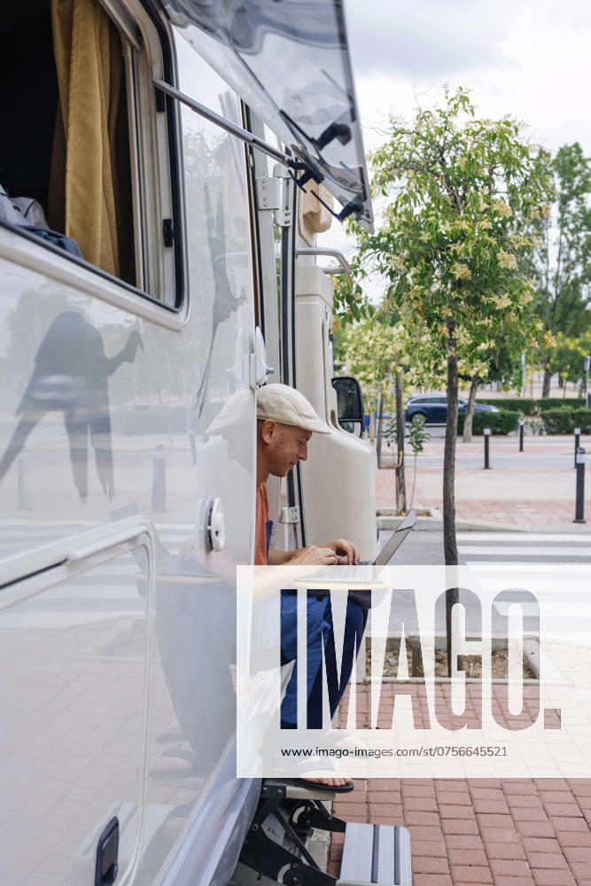 Freelancer using laptop and sitting on doorway of motor home near sidewalk model released, Symbolfoto property released, JCMF02416
