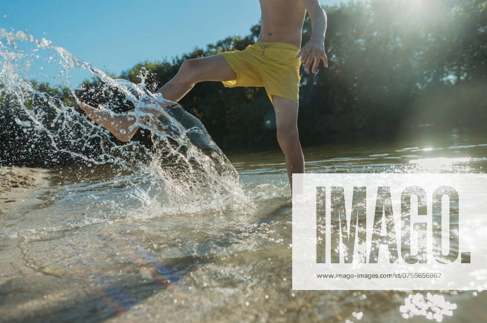 Playful boy kicking and splashing water at river on sunny day model released, Symbolfoto, ANAF03623