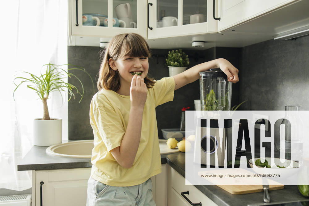Smiling girl eating spinach leaf and making smoothie in kitchen at home model released, Symbolfoto property released, ELMF00669