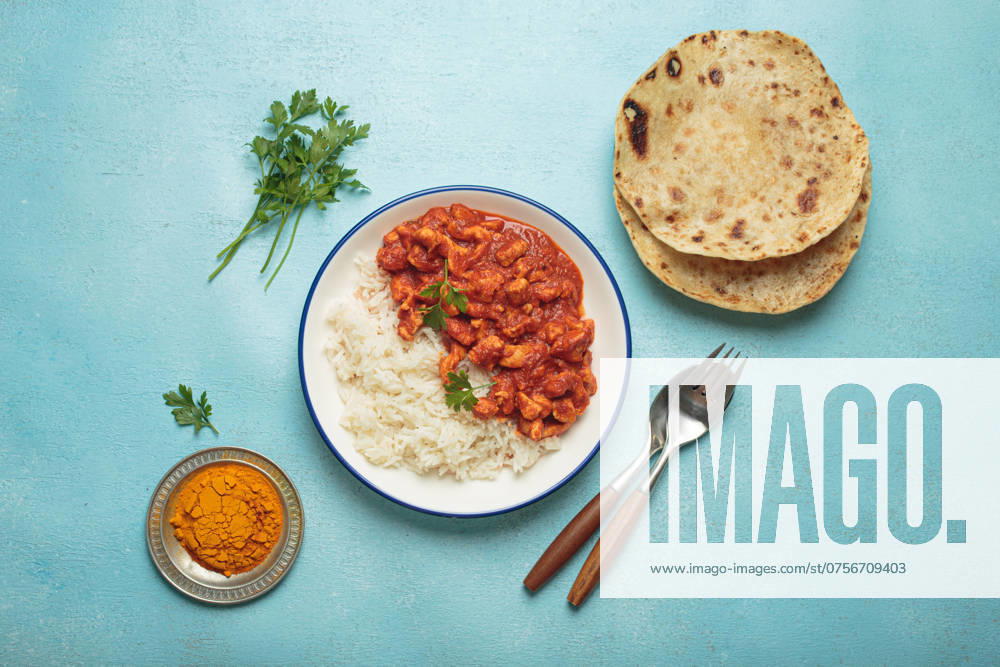 IMAGO Creative, Food, Brot, Naan Indian chicken curry with basmati rice served on plate with chapati flatbread on the side top view Delicious chicken curry with basmati rice, chapati, and cutlery on blue background. Top view shows homemade Indian meal. Spicy and tasty for lunch or dinner