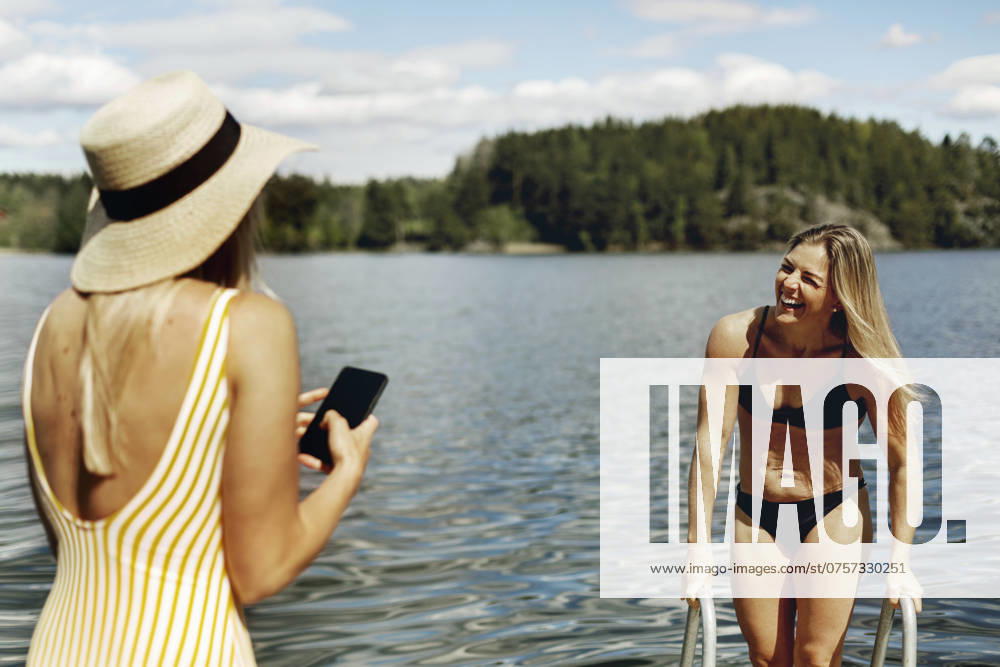 Woman photographing friend while bathing in lake , model released