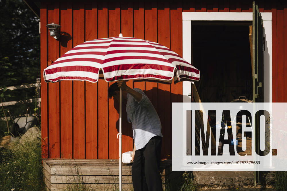 Man unfolding parasol in front of shed , model released , property released