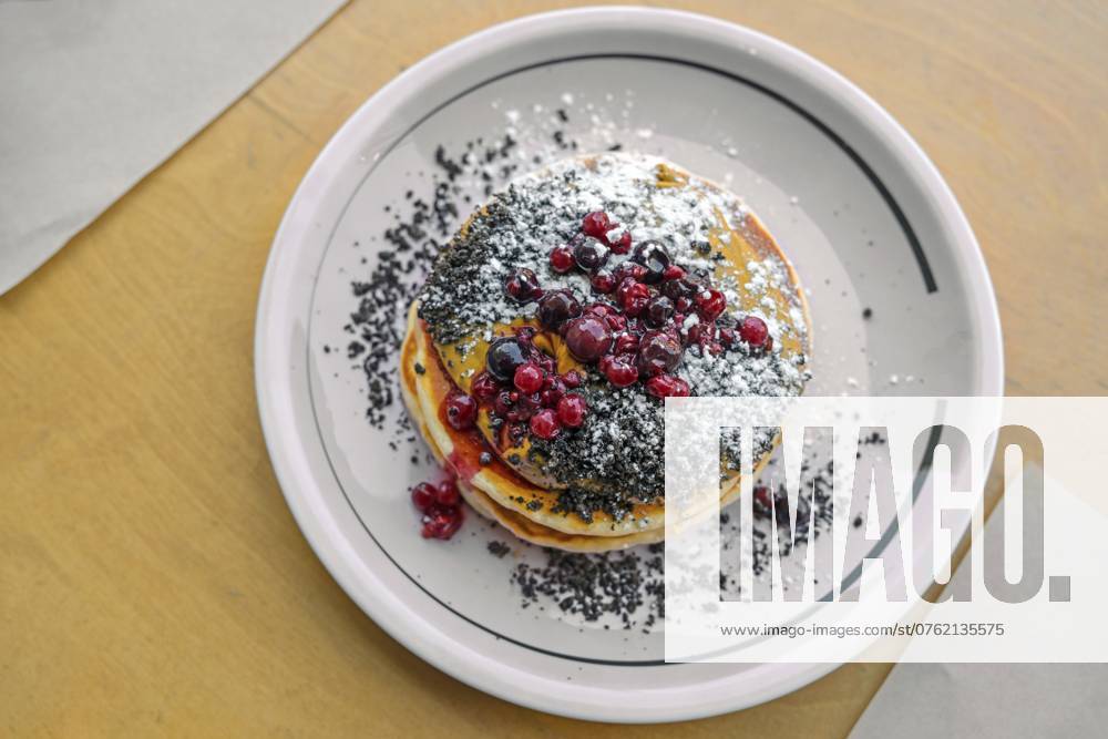 Pfannkuchen mit Erdnussbuttercreme, Beeren, Streuseln und Puderzucker auf einem Teller und einem Holztisch, süßes Brunch oder Dessertgericht, Draufsicht von oben, Kopierraum, gewählter Fokus, enge Tiefenschärfe Pancakes with peanut butter cream, berries, crumble and icing sugar on a plate and a wooden table, sweet brunch or dessert dish, top view from above, copy space, selected focus, narrow depth of field