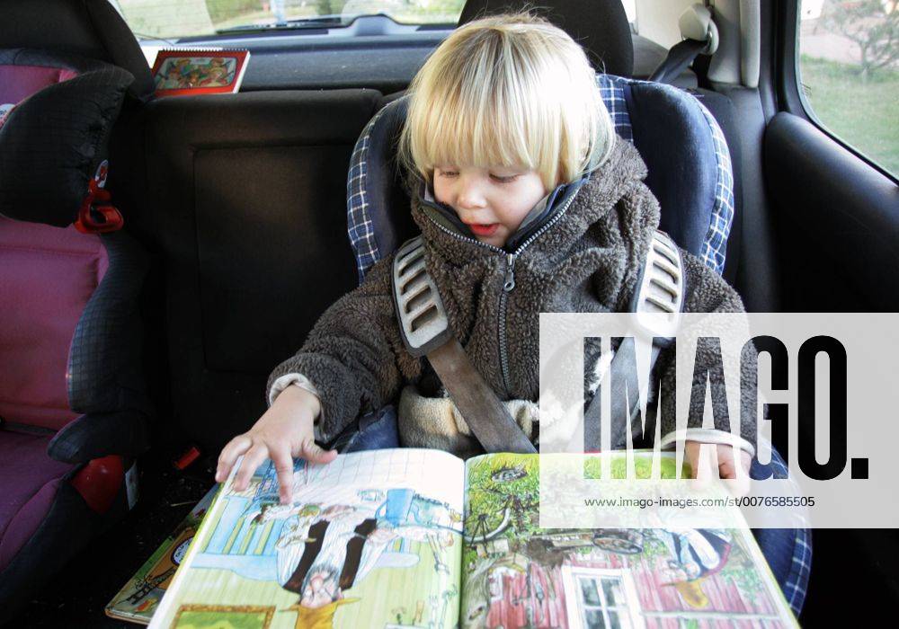 Zingst, Mecklenburg-Vorpommern, DEU - Ein Kleinkind im Kindersitz schaut sich ein Buch an. (Mensch, Kind, Kleinkind, Kindheit, Junge, Maedchen, Knabe, Bube, Kindersitz, Sitz, Auto, Ruecksitz, Autofahrt, autofahren, Sicherheit, angeschnallt, anschnallen, sichern, Fuersorgepflicht, Buch, Bilderbuch, ansehen, lesen, anschauen, Alltag, Emotion, Mimik, konzentriert, Konzentration, Gesellschaft, Innenaufnahme, Rueckbank, Reise, reisen, Urlaub, Ferien, Ausflug, Verkehr, Autosicherheit, Anschnallpflicht, Verkehrssicherheit, Gurt, Sicherheitsgurt, Gurte, Automobil, Gurtpflicht, Unfall, Unfallvermeidung, Verletzung, Verletzungsvermeidung, Unfallverhuetung, digital, QF, Unfallverhütung, Mädchen, Rücksitz, Fürsorgepflicht) 00S051121D001.JPG MODEL RELEASE: YES MR:Y