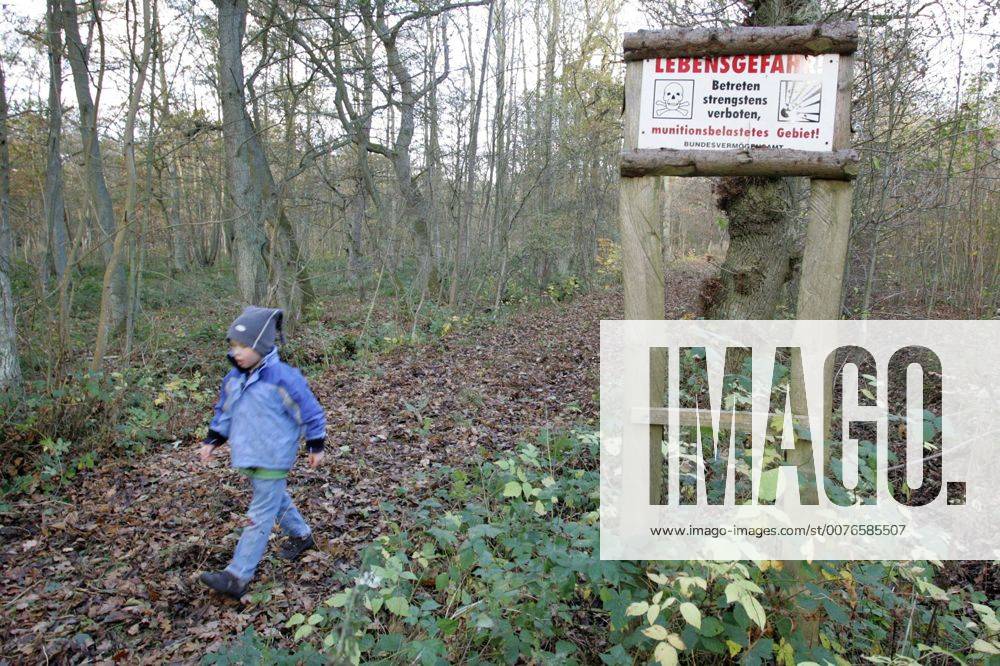 Zingst, Mecklenburg-Vorpommern, DEU - Ein Kind laeuft auf einem Waldweg mit Hinweisschild Lebensgefahr. (Mensch, Kind, Junge, Maedchen, Kindheit, Bube, Knabe, Gesellschaft, Lebenswelt, Lebenswelten, Freizeit, Urlaub, Reise, Tourismus, Schild, Aufsichtspflicht, gehen, laufen, wandern, Wanderung, Weg, Pfad, Waldweg, verboten, Jahreszeit, Herbst, Laub, Herbstlaub, Warnschild, Warnung, Verbot, Verbotsschild, Hinweis, Lebensgefahr, Gefahr, gefaehrlich, Totenkopf, Staat, Bund, Bundesvermoegensamt, Blindgaenger, Bombe, Bomben, Granaten, Munition, munitionsbelastet, Sprengplatz, Sprengung, sprengen, Hinterlassenschaft, Hinterlassenschaften, Krieg, Kriegsfolgen, Kriegshinterlassenschaft, Kriegshinterlassenschaften, Mine, Minen, Landmine, Landminen, Minenfeld, Minenfelder, Militaer, militaerisch, Aussenaufnahme, Hinweisschild, digital, QF, gefährlich, Bundesvermögensamt, Blindgänger, M MR:N