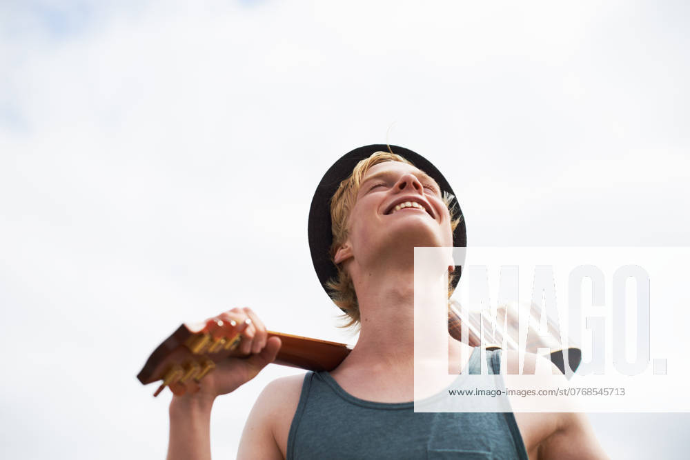Freedom, sky and man with guitar, smile and inspiration in nature for talent, journey and vacation. Artist, musician or guitarist with creative thinking, music and travel adventure with happy holiday. model released property released