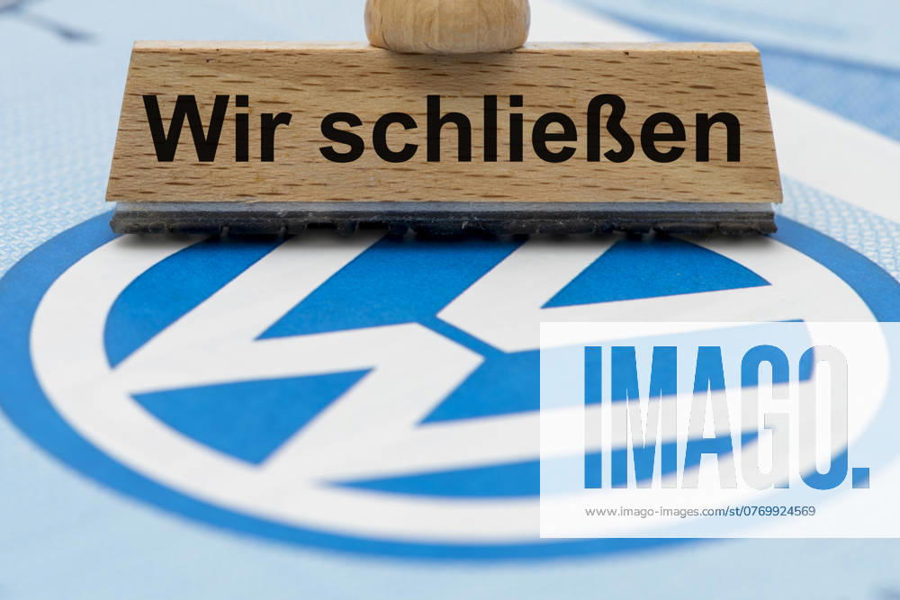 VW-Krise mit Gefahr der Werksschließung Ein Holzstempel ist beschriftet mit dem Aufdruck: Wir schließen, über einer VW-Aktie mit Logo - Symbolbild
