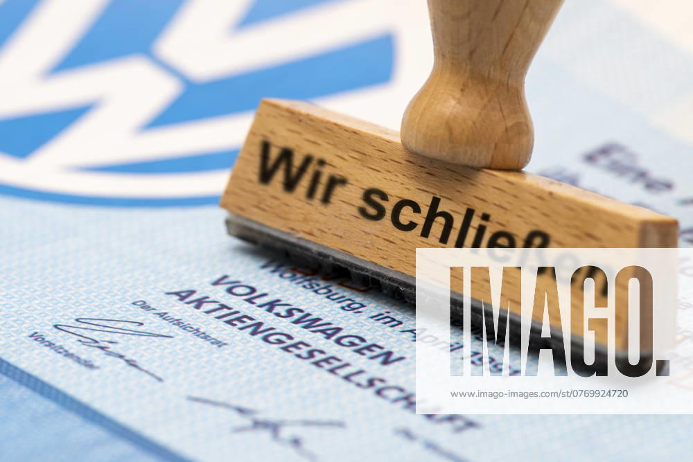 VW-Krise mit Gefahr der Werksschließung Ein Holzstempel ist beschriftet mit dem Aufdruck: Wir schließen, über einer VW-Aktie mit Logo - Symbolbild