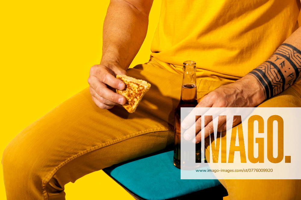 A vibrant scene featuring a man dressed in a yellow suit, holding a piece of Spanish tortilla and a bottle of beer, against a monochrome yellow background Model Released SergioVictorVega_ID24526_711158_021