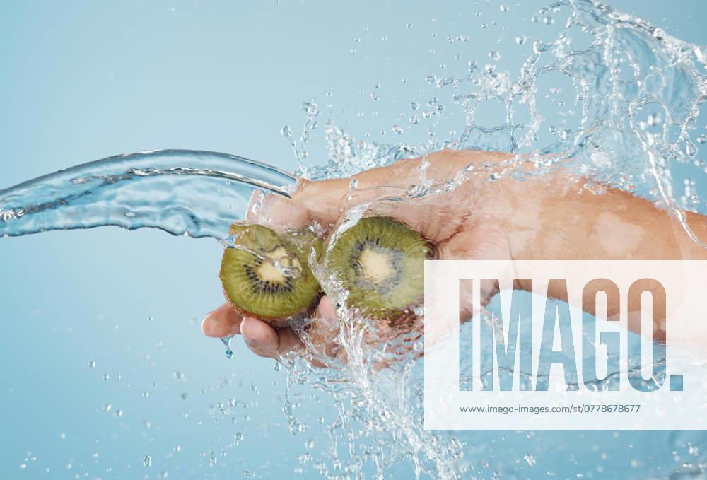 Hands, beauty and kiwi in a studio with splash for skincare, shower and organic treatment against a blue background. Hand, water and fruit with woman wellness model grooming, hygiene and cleaning. model released property released