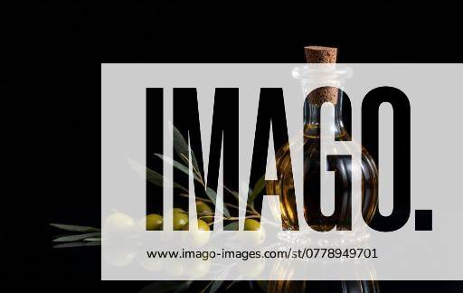 Elegant glass bottle of olive oil with fresh olives and leaves on a reflective surface against a black background. 27085462 RECORD DATE NOT STATED