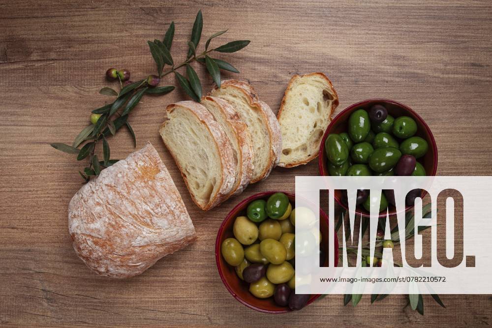 Eine Mischung aus Oliven, Sorten von Chalkidiki, Verdi giganti und Kalamata, in einer Schale, mit geschnittenem Ciabata Brot, Ansicht von oben, ohne Personen A mixture of olives, varieties of Halkidiki, Verdi giganti and Kalamata, in a bowl, with sliced ciabata bread, top view, no people