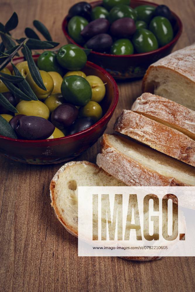 Eine Mischung aus Oliven, Sorten von Chalkidiki, Verdi giganti und Kalamata, in einer Schale, mit geschnittenem Ciabata Brot, Ansicht von oben, ohne Personen A mixture of olives, varieties of Halkidiki, Verdi giganti and Kalamata, in a bowl, with sliced ciabata bread, top view, no people