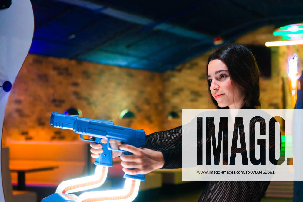IMAGO Creative, Lifestyle, Gaming A focused young woman enjoys an intense arcade experience, holding a blue plastic gun The vibrant arcade setting enhances the excitement and immersive experience Model Released NataliaPenado_ID25228_729722_015