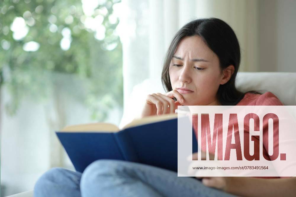 Sad asian woman reading a paper book on a couch, Sad asian woman reading a paper book sitting on a couch at home, Sad asian woman reading a paper book sitting on a couch at home model released, Symbolfoto , 02.12.2024,