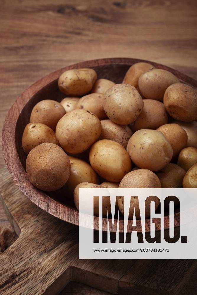 Kleine, ungeschälte Kartoffeln, die in einer rustikalen Holzschüssel versammelt sind, heben ihre erdige Textur und ihre natürlichen Farben vor einem warmen Holzhintergrund hervor Small, unpeeled potatoes gathered together in a rustic wooden bowl, highlighting their earthy texture and natural colors against a warm wooden backdrop.