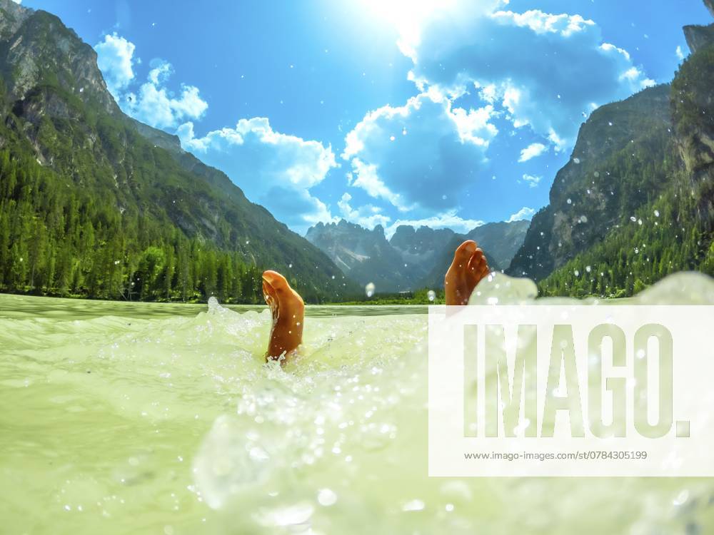 Füße eines Touristen, der im türkisfarbenen Wasser des Lago di Landro oder Durrensees plantscht, mit den Dolomiten im Hintergrund, im Sommer, Italien, Europa Feet of a tourist splashing in the turquoise water of lago di landro or durrensee lake, with the dolomites mountains in the background, in summer, italy