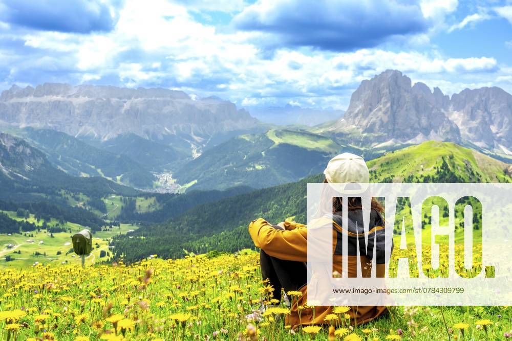 Wanderer, der im Sommer die atemberaubende Aussicht auf die Seceda Berge in den Dolomiten genießt, umgeben von bunten Wildblumen Hiker enjoying the stunning view of the seceda mountains in the dolomites during summer, surrounded by colorful wildflowers