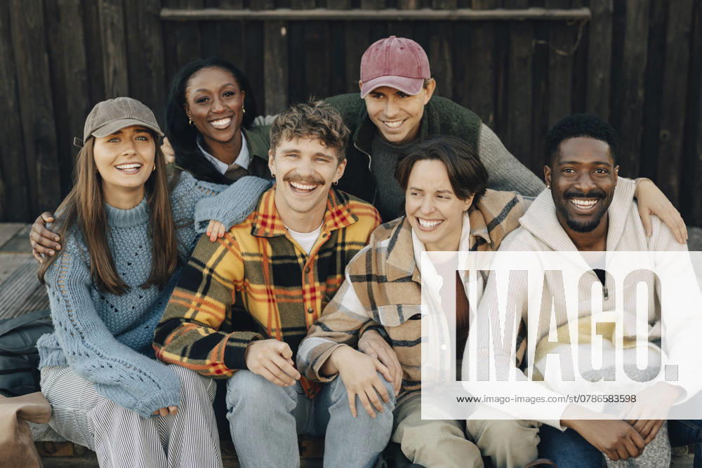 Portrait of happy multiracial male and female friends sitting with arm around each other Sweden, Gothenburg, model released, property released