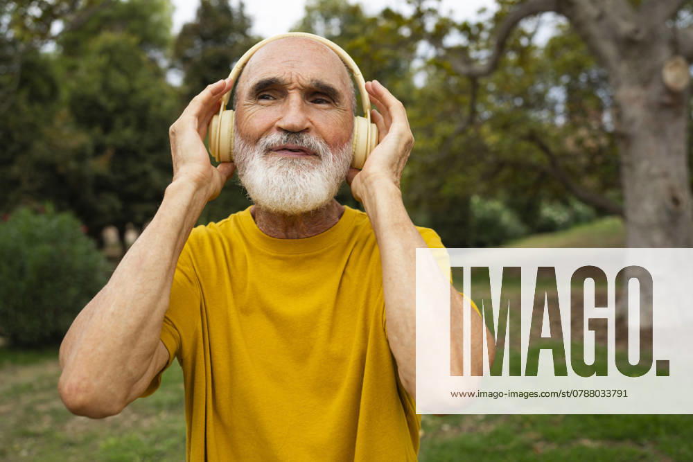 Happy senior man listening to music through wireless headphones in park model released, Symbolfoto, OGSF00136