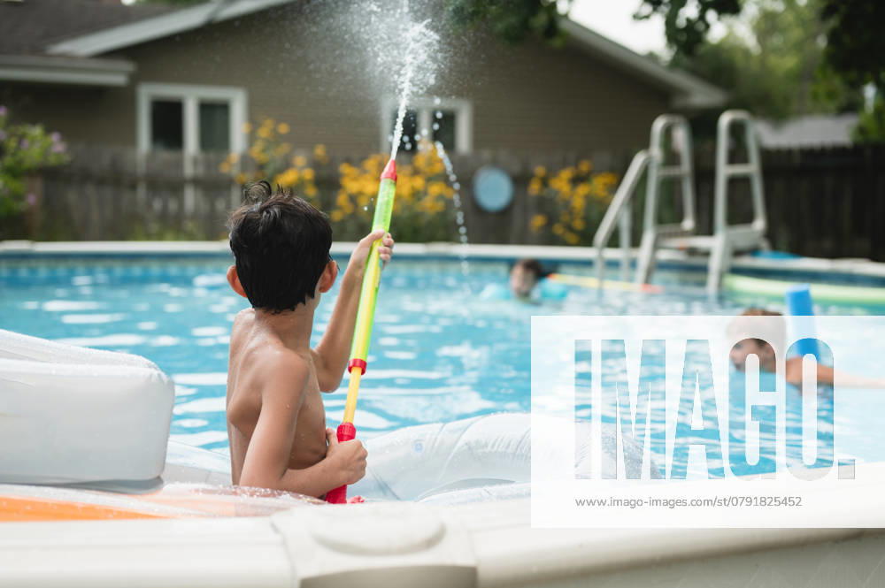 IMAGO Creative, Sommer, Sommertage im Garten IMAGO Creative, Jahreszeit Sommer, Sommerferien Backview of child spraying water toy in pool with other kids swimming Chicago, Illinois, United States CR_AKAO250103-1506409-01 ,model released, Symbolfoto