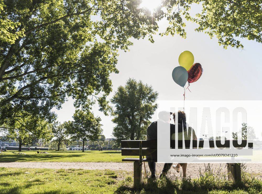 Happy senior couple with balloons sitting on bench in a park model released Symbolfoto UUF10649