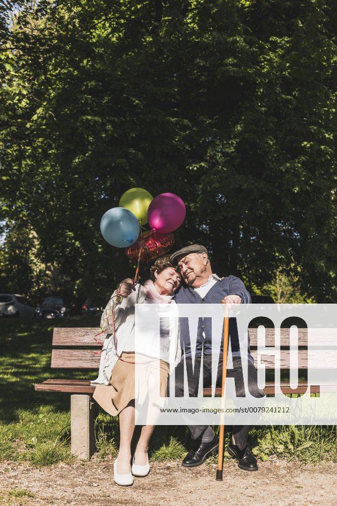 Happy senior couple with balloons sitting on bench in a park model released Symbolfoto UUF10651