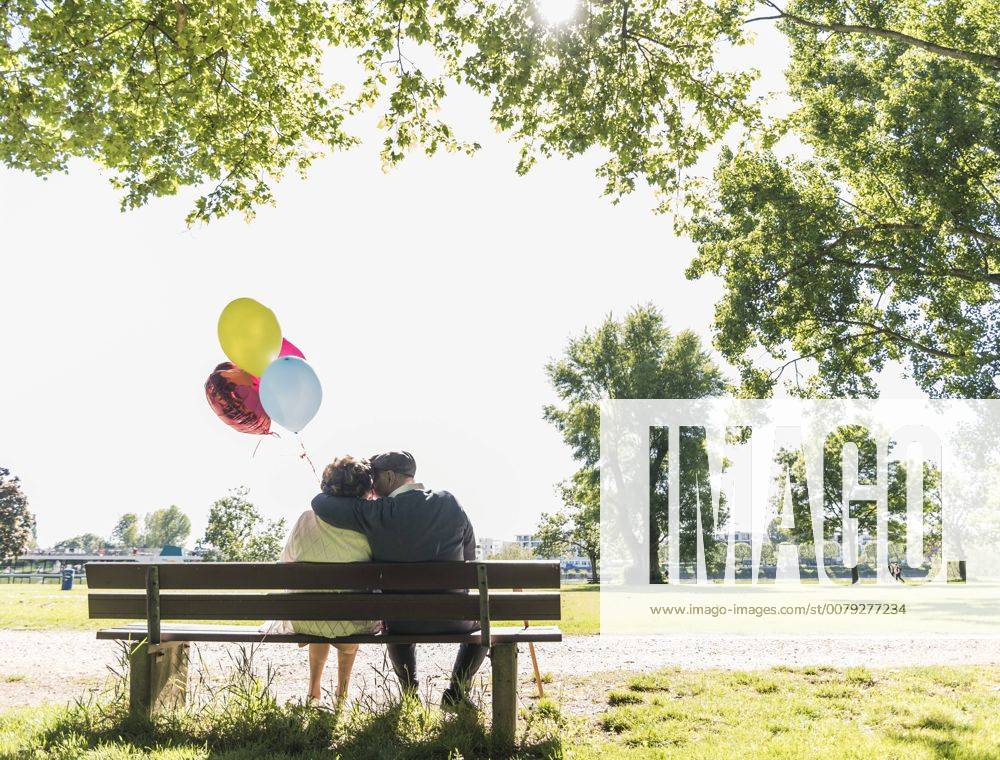 Happy senior couple with balloons sitting on bench in a park model released Symbolfoto UUF10648