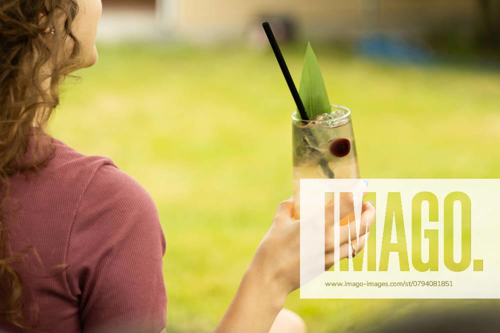IMAGO Creative, Jahreszeit Sommer, Kirschen A woman holds a refreshing cocktail with a black straw and garnish while relaxing outdoors The scene captures a leisurely summer moment, embodying relaxation and enjoyment Model Released Ptashkimenko_ID25739_742568_007