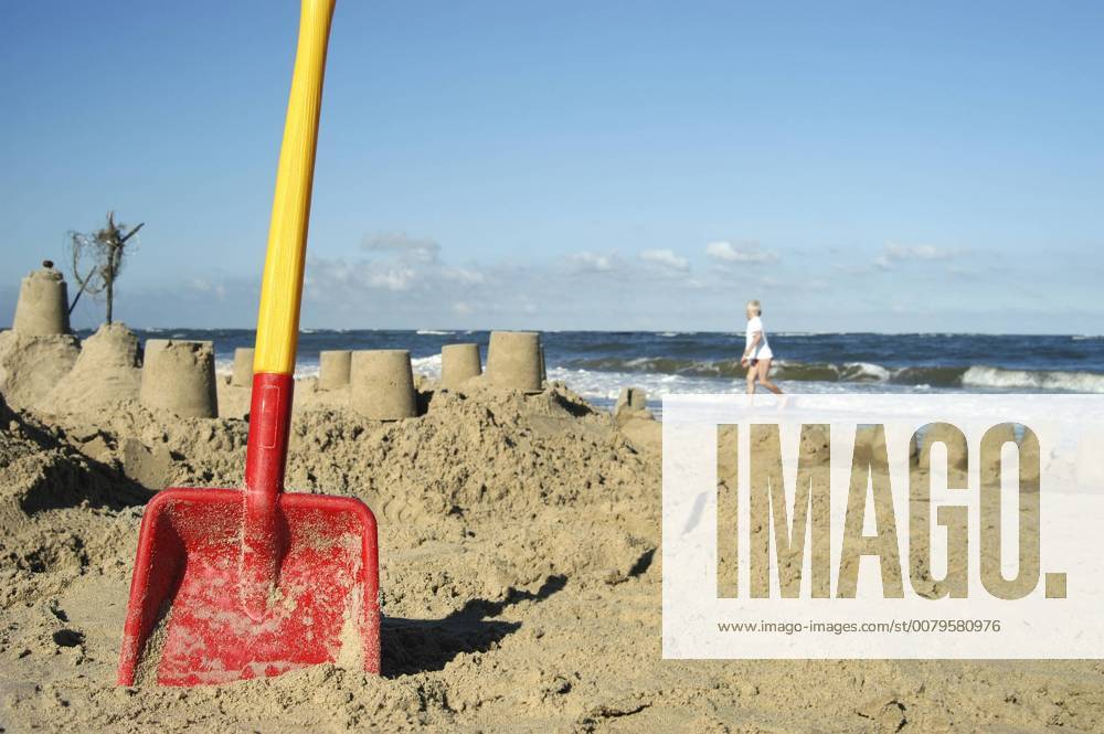 Eine rote Schaufel steckt am Strand im Sand nach dem Bau einer großen Sandburg Strandvergnügen