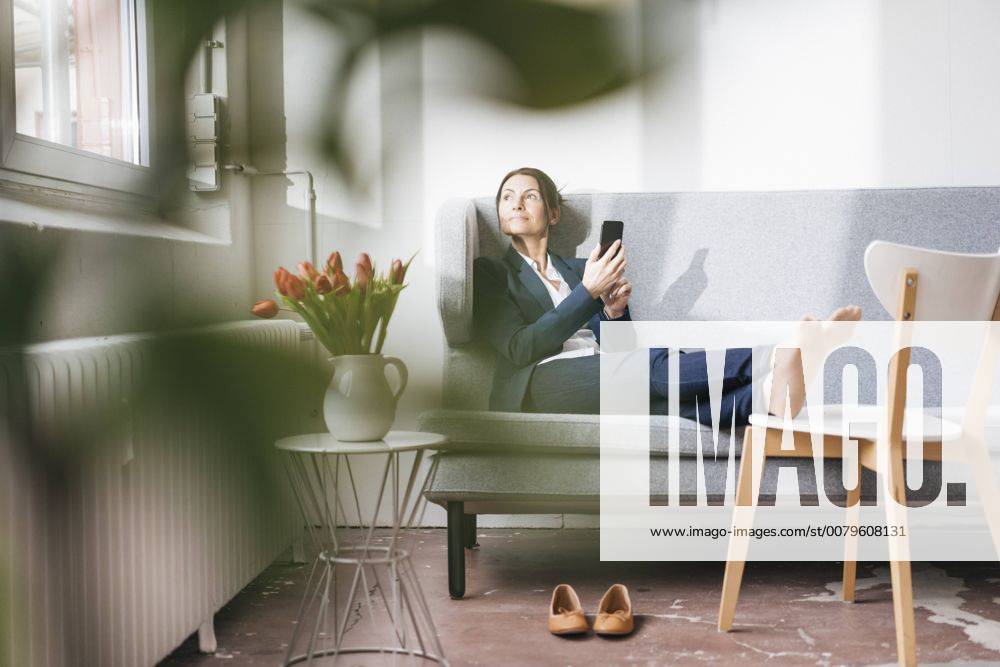 Businesswoman sitting on couch in a loft looking out of the window model released Symbolfoto property released JOSF01171