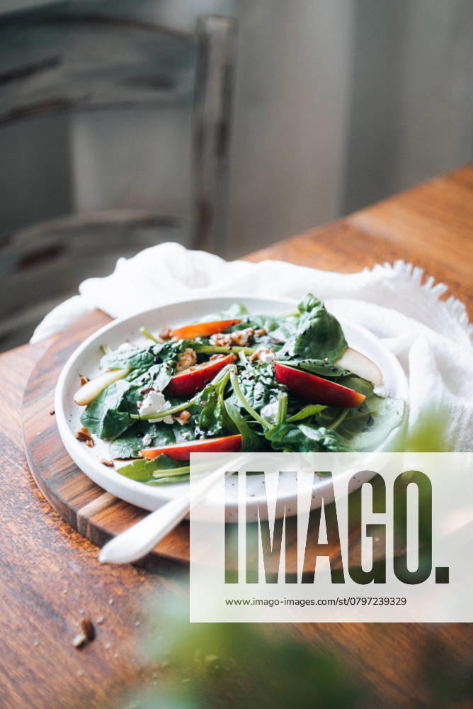 A wholesome dish featuring fresh spinach leaves, crisp apple slices, and crunchy pecan nuts, garnished with sesame seeds, served on a white plate. Model Released CamilaMacedo_ID26018_750702_003