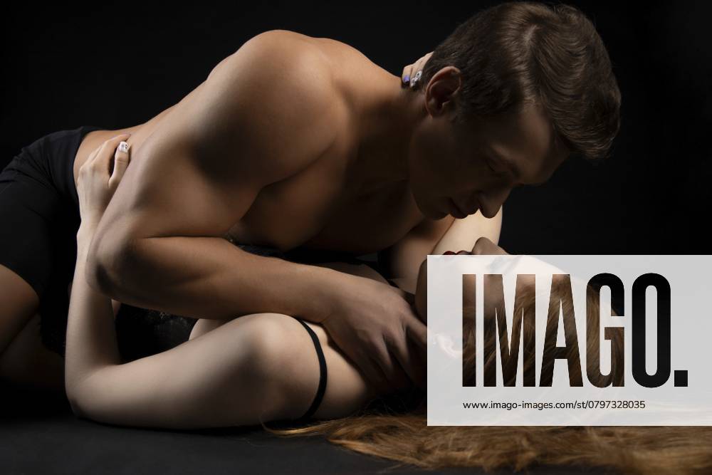 Seitenansicht einer jungen Frau in schwarzen Dessous, die einen Mann bei erotischen Spielen in einem dunklen Studio dominiert Side view of young female in black lingerie dominating man during erotic games in dark studio
