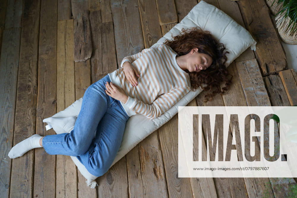 IMAGO Creative, Gesellschaft, Leisure Sickness Schöne junge ruhige Frau schläft, Nickerchen während des Tages auf Matratze auf Holzboden in gemütlichen Haus Beautiful young calm Italian woman lying on mattress on wooden floor at home, peaceful Hispanic female sleeping, napping, getting some rest during day, top view, full length image. Napping Meditation ,model released, Symbolfoto