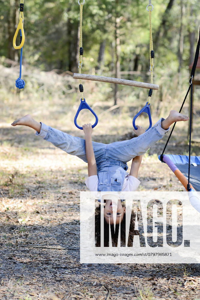 IMAGO Creative, Sommer, Sommertage im Garten A playful child in overalls hangs upside down on a rope swing ou United States, Florida, Inverness R_YWQX250124-1637055-01 ,model released, Symbolfoto